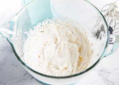 a glass bowl filled with whipped cream on top of a marble counter next to utensils