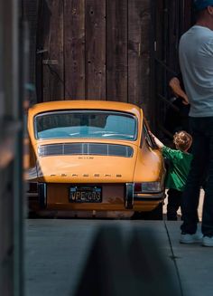 a man standing next to a yellow car with a little boy in front of it