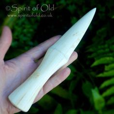 a hand holding a small white object in it's left hand, with green plants behind it