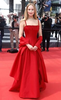 a woman in a red dress standing on a red carpet with cameras taking pictures behind her