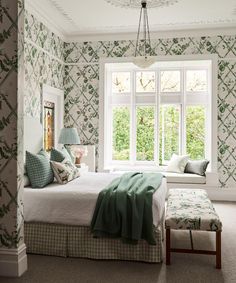 a bed sitting under a window next to a white chair and ottoman in a bedroom