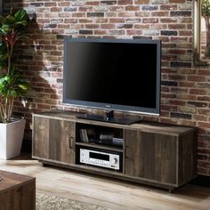 a flat screen tv sitting on top of a wooden entertainment center in front of a brick wall