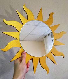 a hand holding up a mirror with the reflection of a sun on it's side