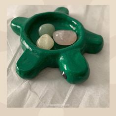 a small green ceramic bowl with three stones in it and the lid is shaped like a turtle