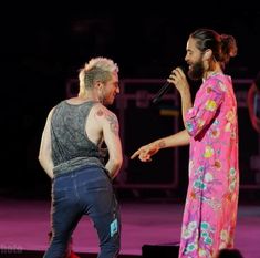 two men on stage with one holding a microphone and the other wearing a pink robe