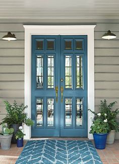 a blue front door with two potted plants on the side and an area rug