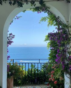 an archway with flowers and plants on the outside, looking out onto the ocean from a patio