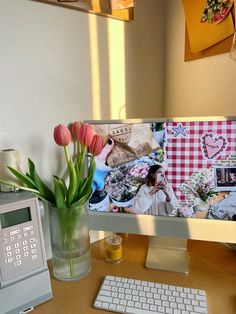 a computer monitor sitting on top of a desk next to a vase with flowers in it