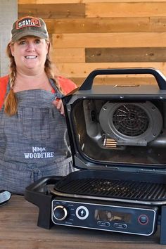 a woman in an apron and hat standing next to a grill with the lid open