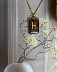 a necklace with the letter h on it hanging from a tree branch in front of a window