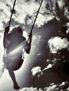 a woman is swinging on a rope in the air with clouds behind her and sun shining through