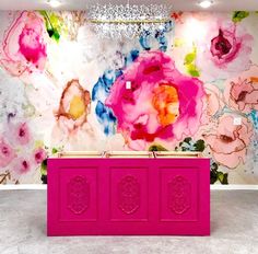 a pink counter sitting in front of a wall with flowers on it and chandelier hanging from the ceiling