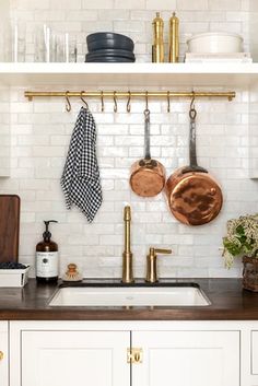 a kitchen with white brick walls and gold accessories on the rack above the sink, along with copper pots and pans