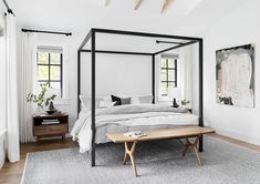 a white bedroom with four poster bed and wooden coffee table in the corner on carpeted floor