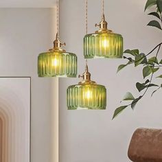 three green glass pendant lights hanging from a ceiling in a living room with a chair and potted plant