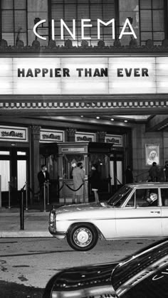 an old car parked in front of a movie theater