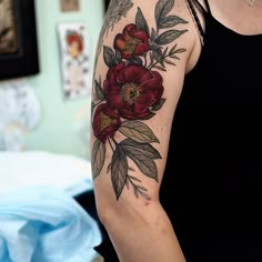 a woman's arm with red flowers on it and green leaves around the arm