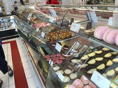 a woman walking past a display case filled with lots of cakes and cupcakes