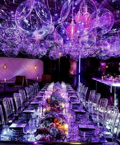 a long table is set up with clear chairs and purple lights hanging from the ceiling