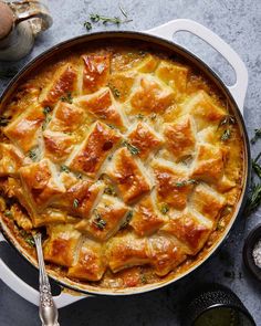 a casserole dish with meat and cheese in it on a gray surface next to some herbs