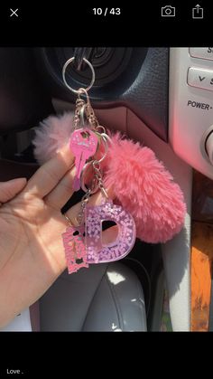 someone is holding two pink keychains in their hand while they are inside the car