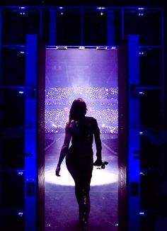 a woman walking down a runway in front of a purple screen with lights on it