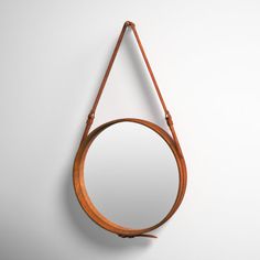 a round mirror hanging on the wall next to a leather strap with a wooden handle