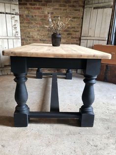 a wooden table with two black legs and a vase on the top, in front of a brick wall