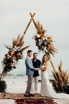 a newly married couple standing under an arch on the beach with flowers and pamodia