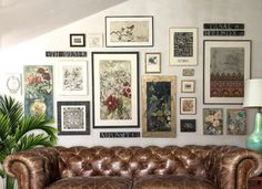 a brown leather couch sitting in front of a wall covered with pictures and framed art