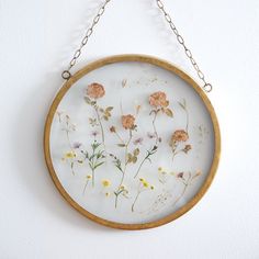 a wooden frame with flowers on it hanging from a chain attached to a white wall