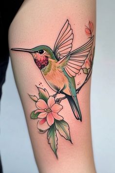 Hummingbird with colorful plumage perched on a branch with pink flowers tattooed on an arm. Hummingbird Tattoo Ideas Female, Hummingbird Tattoo Neo Traditional, Hummingbird Tattoo Colorful, Hummingbird Thigh Tattoo, Hummingbird Tattoo Color, Color Hummingbird Tattoo, Butterfly And Hummingbird Tattoo, Humming Bird Tattoo For Women, Hummingbird Wrist Tattoo