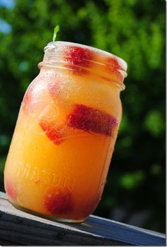 a jar filled with liquid sitting on top of a wooden table next to some trees