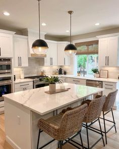 a large kitchen with white cabinets and marble counter tops, two pendant lights over the island