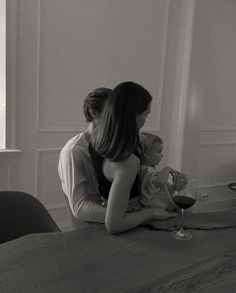 a woman holding a baby while sitting at a table with a glass of wine