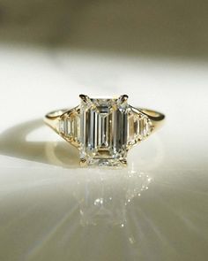 an emerald - cut diamond ring sits on a white surface