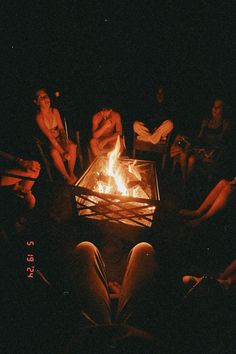 people sitting around a fire pit at night with their feet on the table and legs crossed