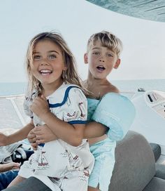 two young children sitting on the back of a boat in the ocean with their arms around each other