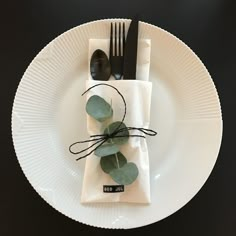 a white plate topped with a fork and knife next to a napkin covered in eucalyptus leaves