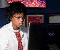 a woman wearing glasses and a tie looking at a laptop