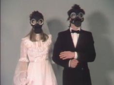 a man and woman wearing gas masks standing next to each other in front of a wall