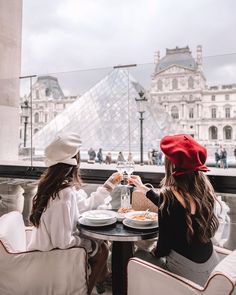 two women sitting at a table with plates of food in front of a glass pyramid