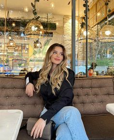 a woman sitting on top of a couch in front of a store window with lights hanging from the ceiling