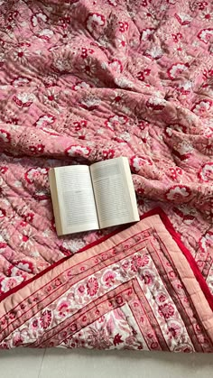 an open book laying on top of a pink quilt