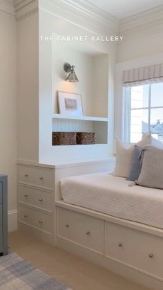 a bedroom with white walls and drawers in the corner, along with a window seat