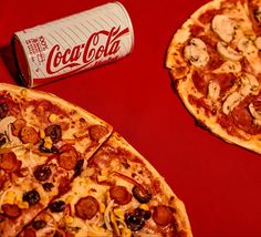 two pizzas with pepperoni and mushrooms next to a can of coca - cola