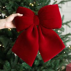 a hand holding a red bow on top of a christmas tree