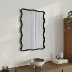 a mirror sitting on top of a wooden dresser next to a potted plant and candle