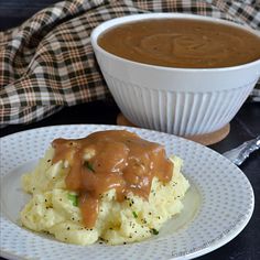 a plate with mashed potatoes covered in gravy next to a bowl of gravy