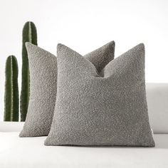 two gray pillows sitting on top of a white couch next to a green cactus plant